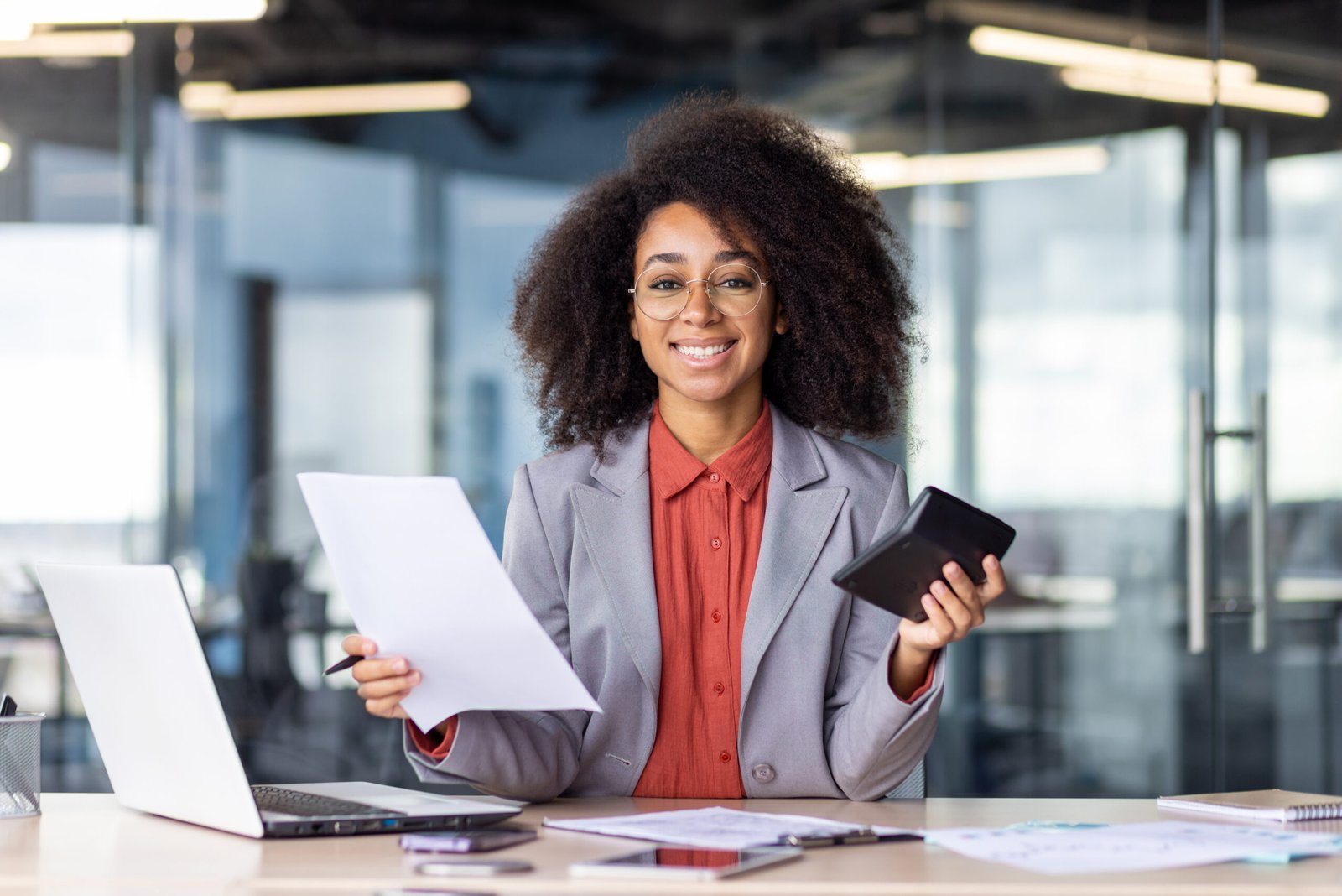Satisfied hispanic lady in orange blouse calculating company budget on electronic device and preparing report. Intelligent accountant finishing massive task with necessary attention to numbers